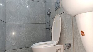 A bathroom with a white toilet, a wall-mounted sink, and grey tiled walls. - Hotel Faaz International (Kannur)