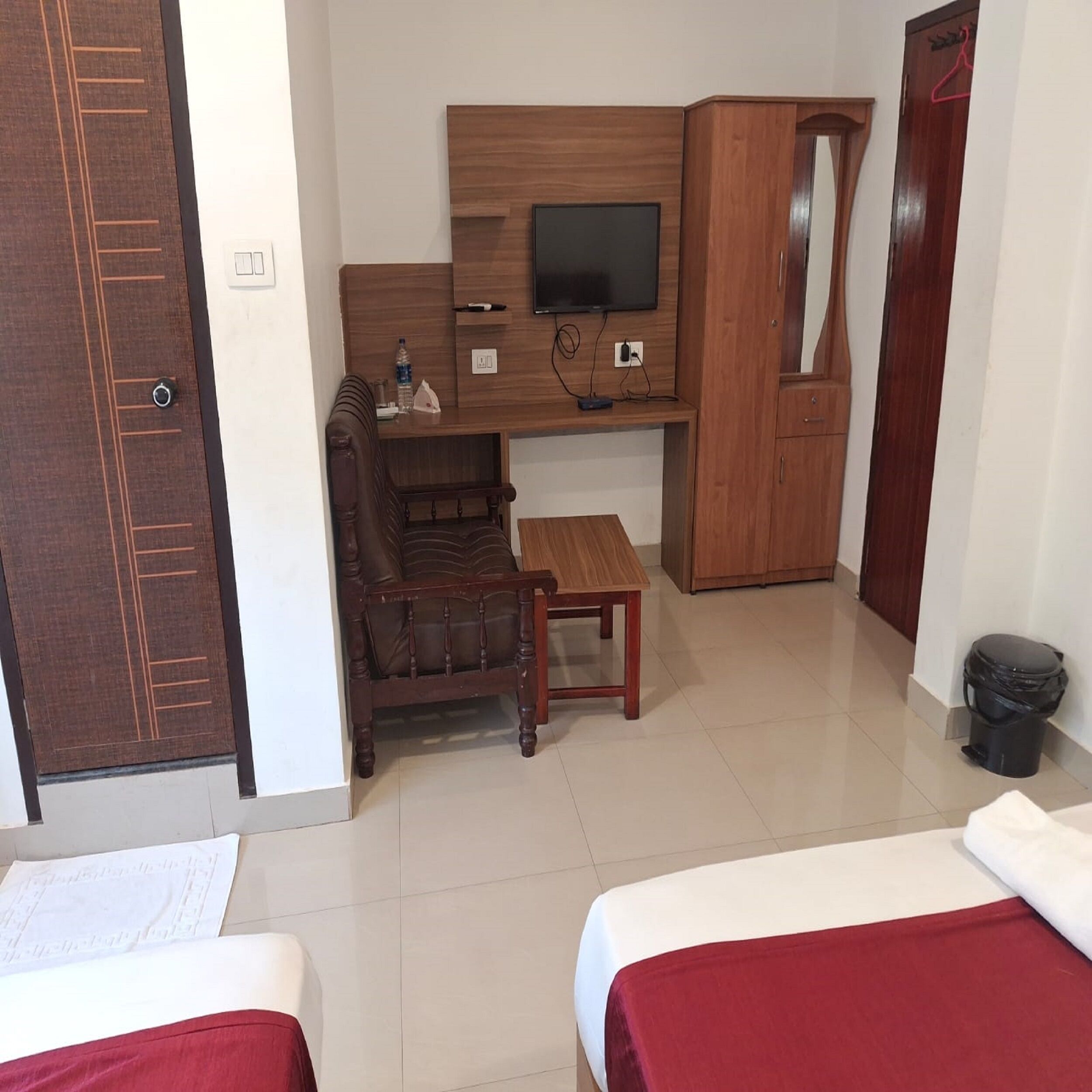 A hotel room with a wooden desk, a chair, a television, and two beds.