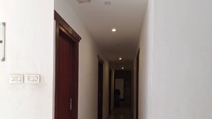 A long, narrow hallway with a wooden door on the left and a white wall with a light switch and socket. - Hotel Faaz International (Kannur)