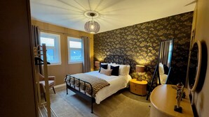 A bedroom with a bed, bedside table, lamp, and a large mirror. - Cochrane House (Stirling)