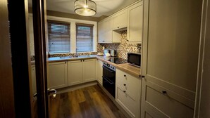 A compact kitchen with a sink, stove, microwave, and a window with blinds. - Cochrane House (Stirling)