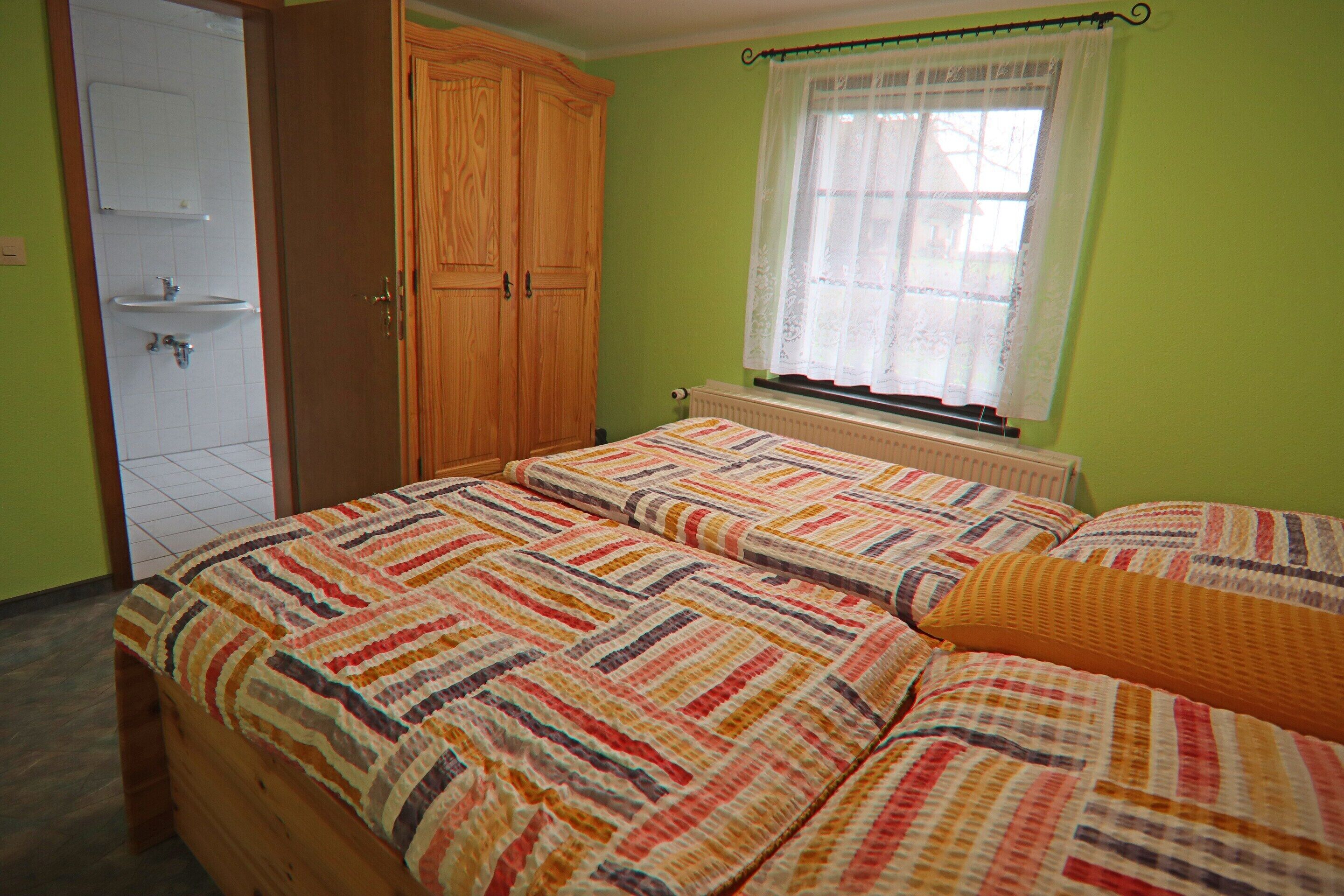 Une chambre avec deux lits, une armoire en bois, une fenêtre avec un rideau et un radiateur.