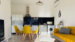 A modern living room with a sofa, a dining table with chairs, a TV, and a kitchen area with a washing machine. - Apartment T2 furnished tourism 2 * air-conditioned near the sea (Olmeto)
