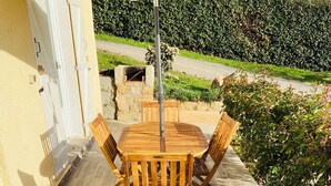 An outdoor patio with a wooden table and chairs, a beige umbrella, and a stone wall in the background. - Apartment T2 furnished tourism 2 * air-conditioned near the sea (Olmeto)