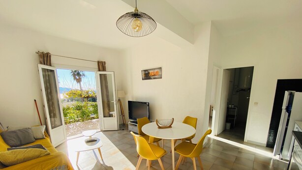 A living room with a sofa, a TV, a dining table with yellow chairs, and a view of the outdoors. - Apartment T2 furnished tourism 2 * air-conditioned near the sea (Olmeto)