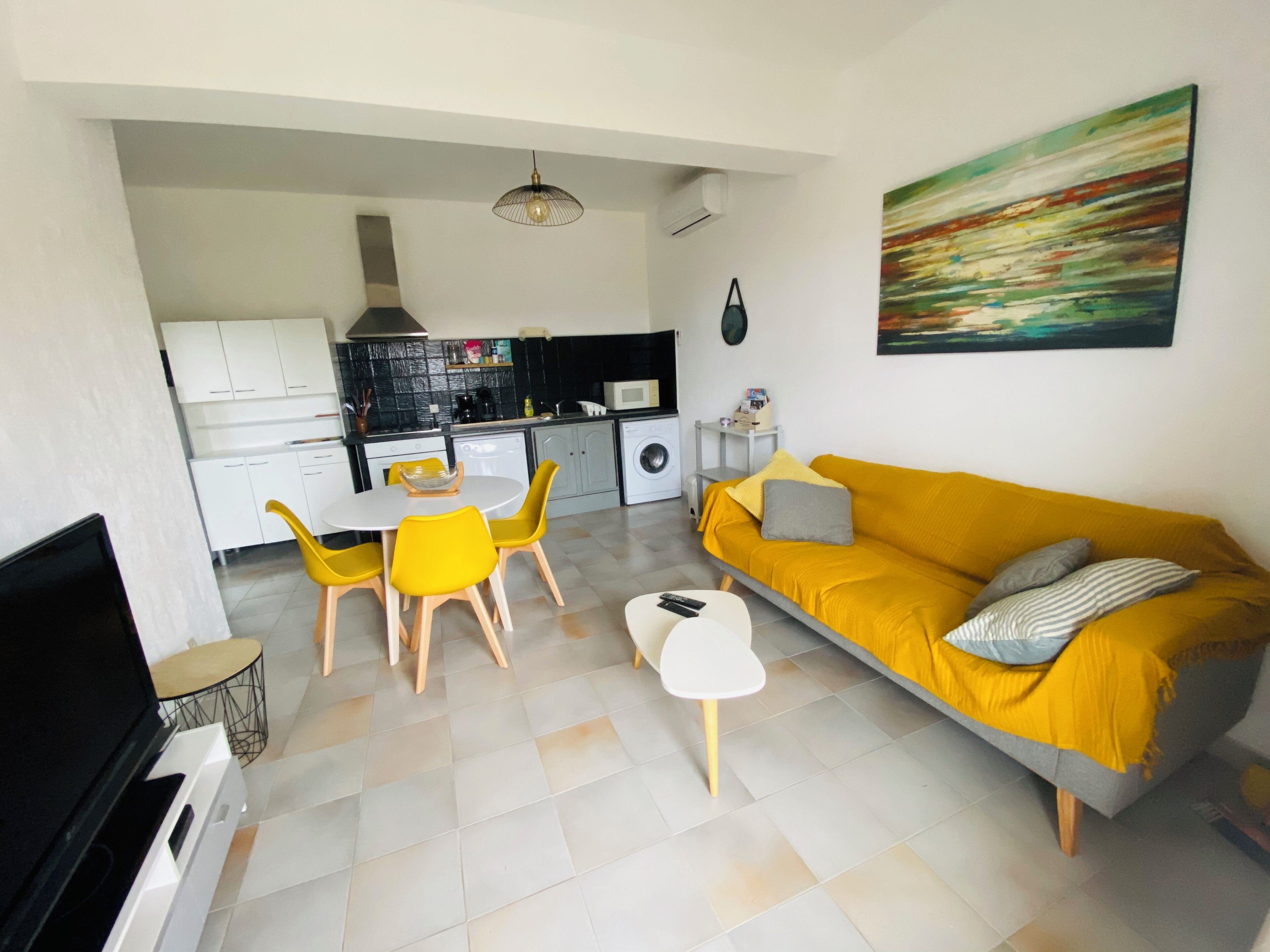 Uma sala de estar moderna com um sofá amarelo, uma área de jantar com cadeiras amarelas e uma cozinha ao fundo.