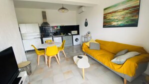 A modern living room with a yellow sofa, a dining area with yellow chairs, and a kitchen in the background. - Apartment T2 furnished tourism 2 * air-conditioned near the sea (Olmeto)