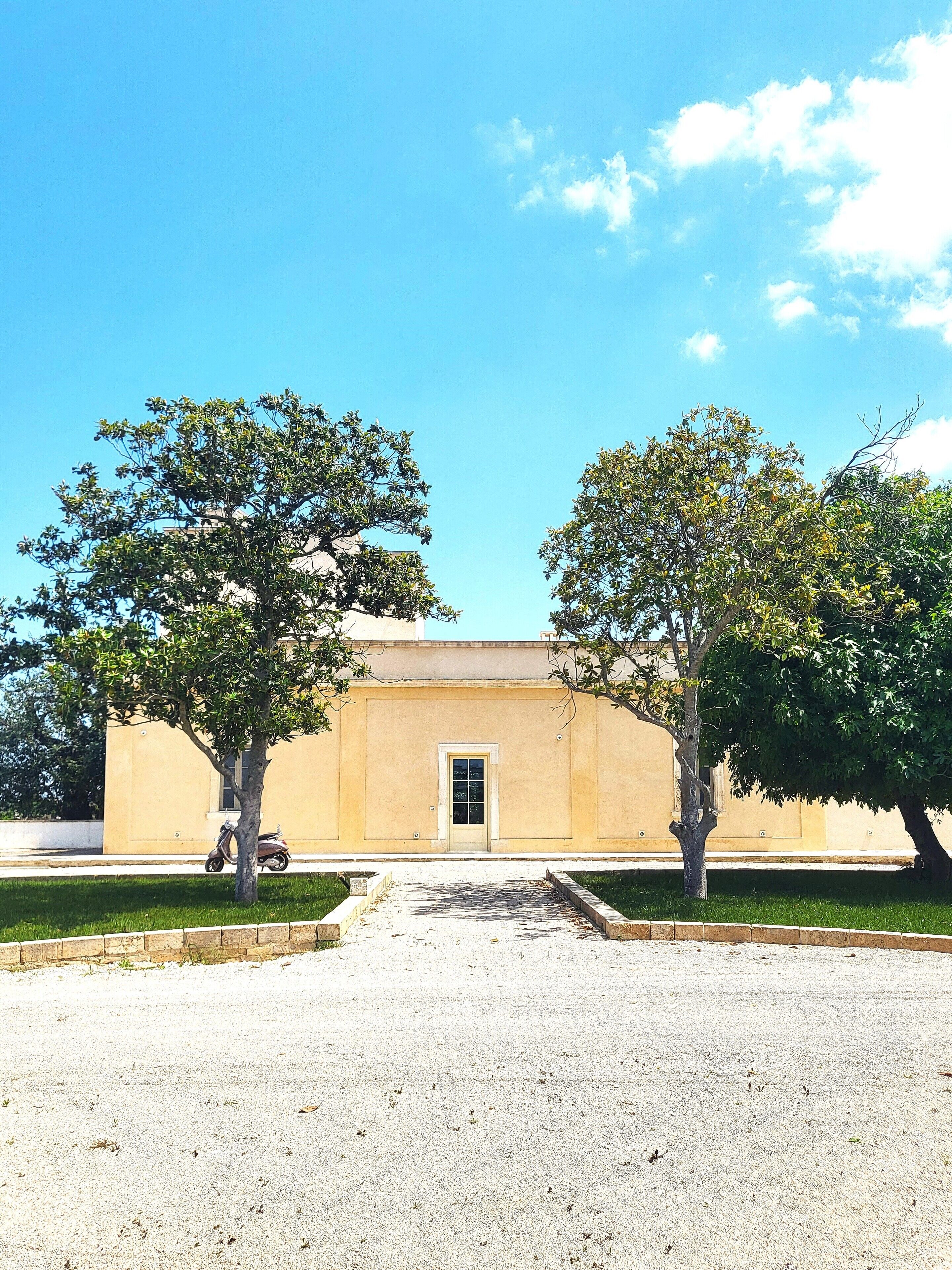 A building with a beige facade, a central door, and two trees in front.