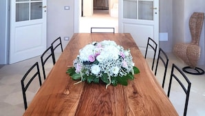 Ein Esszimmer mit einem Holztisch, Stühlen und einer floralen Tischdekoration. Zwei Glastüren und eine Chandelüster sind ebenfalls vorhanden.