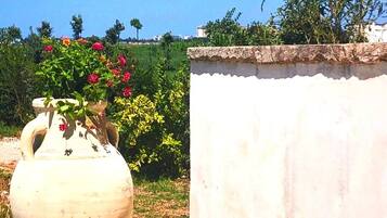 Una maceta blanca de cerámica grande con flores sobre una superficie de concreto, junto a una pared blanca con borde superior texturizado.