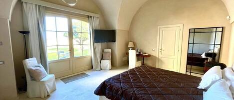 A bedroom with a large bed, a chair, a desk, and a TV.