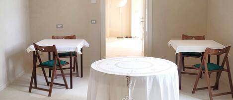 Un comedor con dos mesas, cada una con mantel blanco y sillas de madera. La habitación tiene un techo alto en arco y una puerta que da a otra estancia.