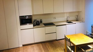 A modern kitchen with white cabinets, a built-in oven, a sink, and a wooden dining table.