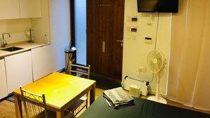 A compact kitchen with a sink, a dining table, and a TV mounted on the wall.