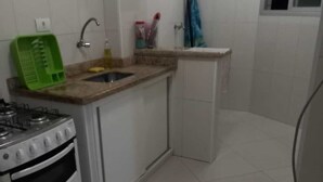 Cocina compacta con armarios blancos, estufa a gas, lavabo y ventana.