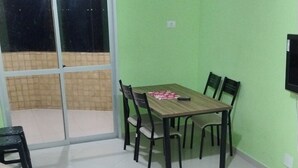 Una sala de estar con un sofá, una mesa de comedor con sillas, un televisor y un ventanal corredizo que da a un balcón.
