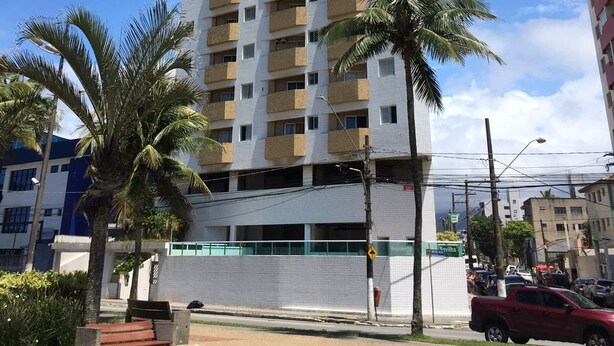 Un edificio de gran altura con varios balcones, rodeado de palmeras y un cielo azul despejado.