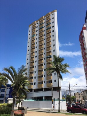 A high-rise building with multiple balconies, surrounded by palm trees and a clear blue sky. - APARTMENT FACING THE SEA, PRAIA GRANDE 🏖️🏖️ (Nova Mirim Praia Grande)