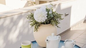 A glass table with a croissant, a teapot, a cup, and a vase with flowers on a rooftop terrace.