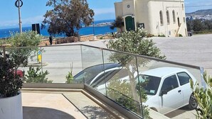 Ein Balkon mit Blick auf eine Küstenlandschaft, ein weißes Auto und ein Gebäude mit einem Turm.