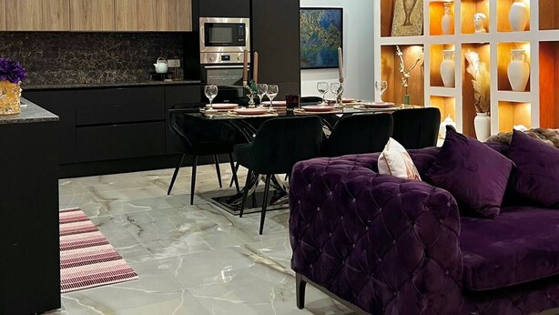 Eine moderne Küche mit integriertem Mikrowellenherd und Backofen, ein Essbereich mit Tisch für vier Personen und ein violettes Sofa im Wohnbereich.