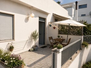 Een balkon met een tafel en stoelen, plantenpotten en een lichtslingering.