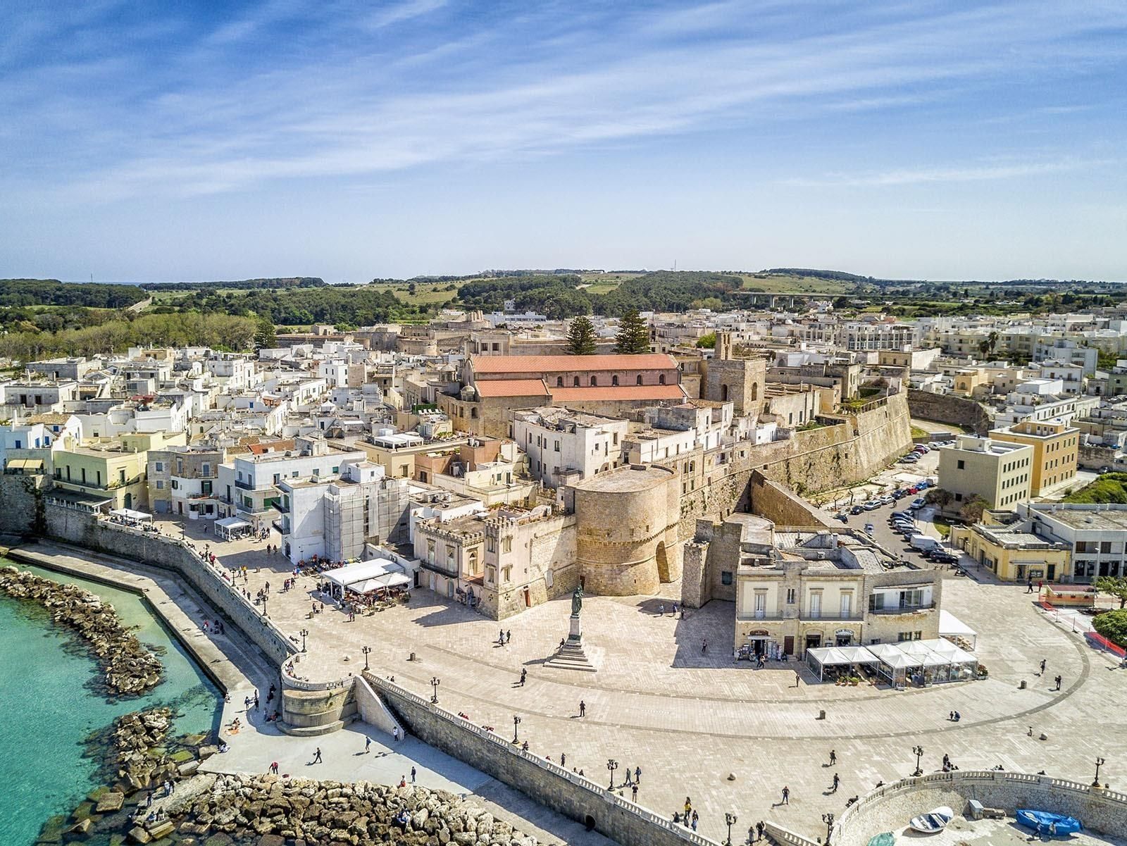 A coastal cityscape with historic architecture, a central square, and a waterfront promenade.