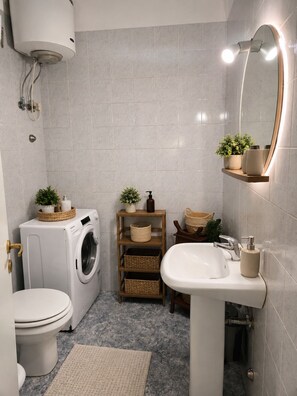 Ein kleines Badezimmer mit Waschmaschine, Toilette, Waschbecken und einem beleuchteten Spiegel.