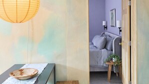 A room with a wooden bench, a small table with a woven basket, and a hanging paper lantern. - Dreamy, Airy 2bd - Senja Suite @ La Dea (Santa Fe)
