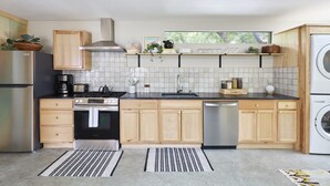 A modern kitchen with wooden cabinets, a stainless steel stove, and a dishwasher. - Dreamy, Airy 2bd - Senja Suite @ La Dea (Santa Fe)