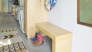 A laundry room with a washing machine, dryer, bench, and a wall-mounted hat rack. - Dreamy, Airy 2bd - Senja Suite @ La Dea (Santa Fe)