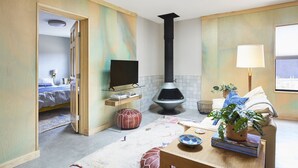 A cozy living room with a television, a fireplace, a sofa, a coffee table, and a potted plant. - Dreamy, Airy 2bd - Senja Suite @ La Dea (Santa Fe)
