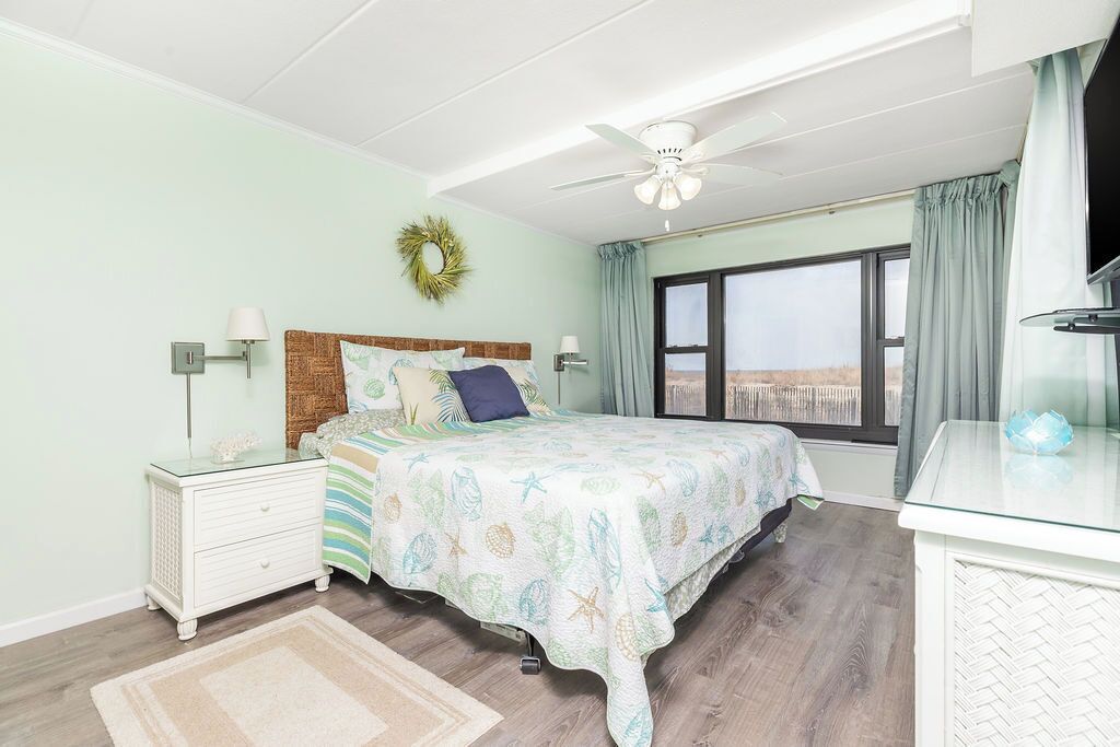 Quarto com cama, mesas de cabeceira, ventoinha no teto, janela com cortinas e vista para o exterior.