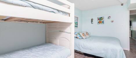 A bunk bed room with a ceiling fan, light blue walls, and a wooden floor.