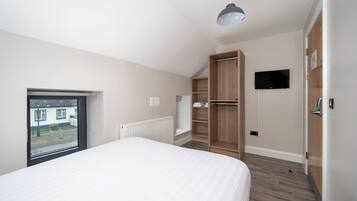 A bedroom with a bed, a window, a wardrobe, a television, and a radiator.