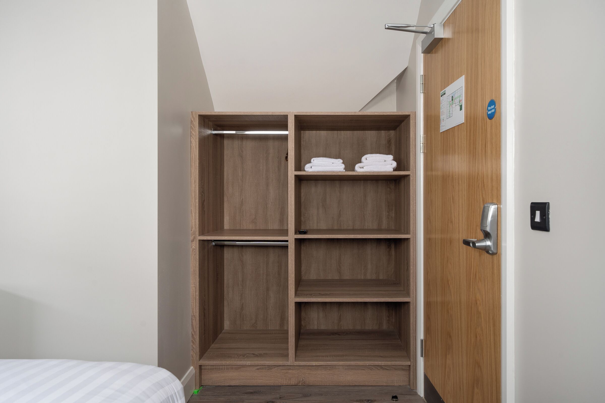 A hotel room with a wooden wardrobe, a bed with a striped bedspread, and a small table.