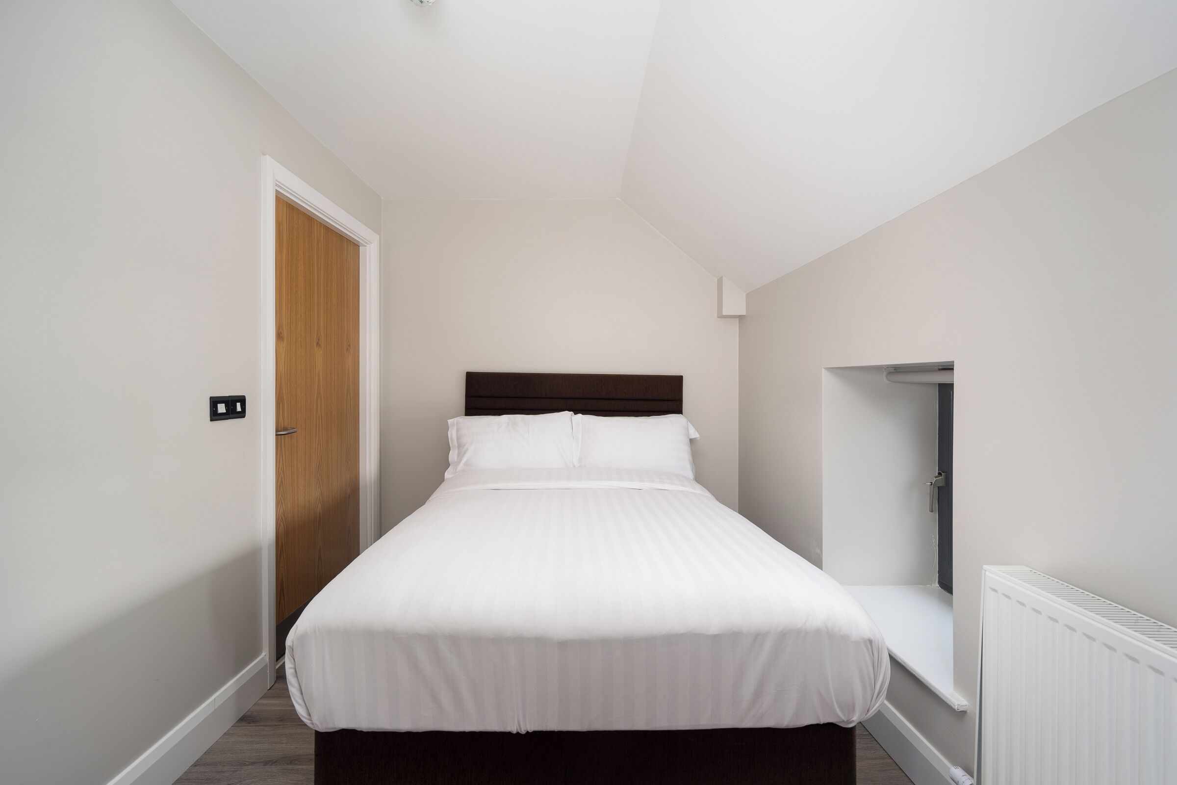 A bedroom with a bed, a wooden door, a white radiator, and a small window.