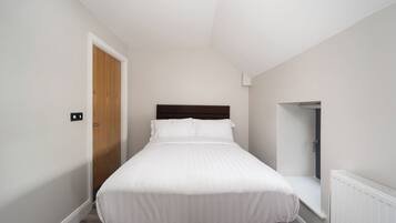 A bedroom with a bed, a wooden door, a white radiator, and a small window.