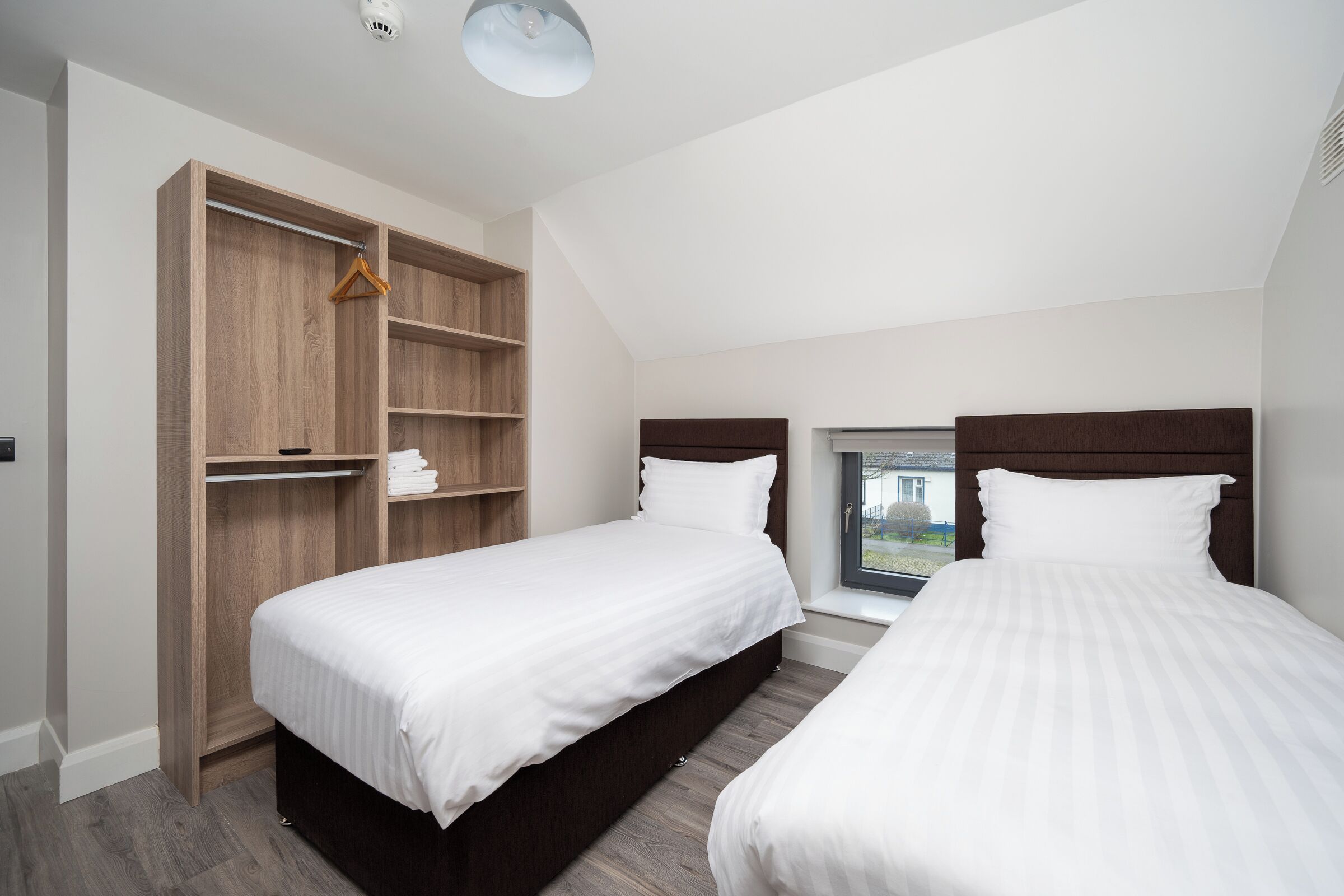 A bedroom with two beds, a wooden wardrobe, and a window with a view.