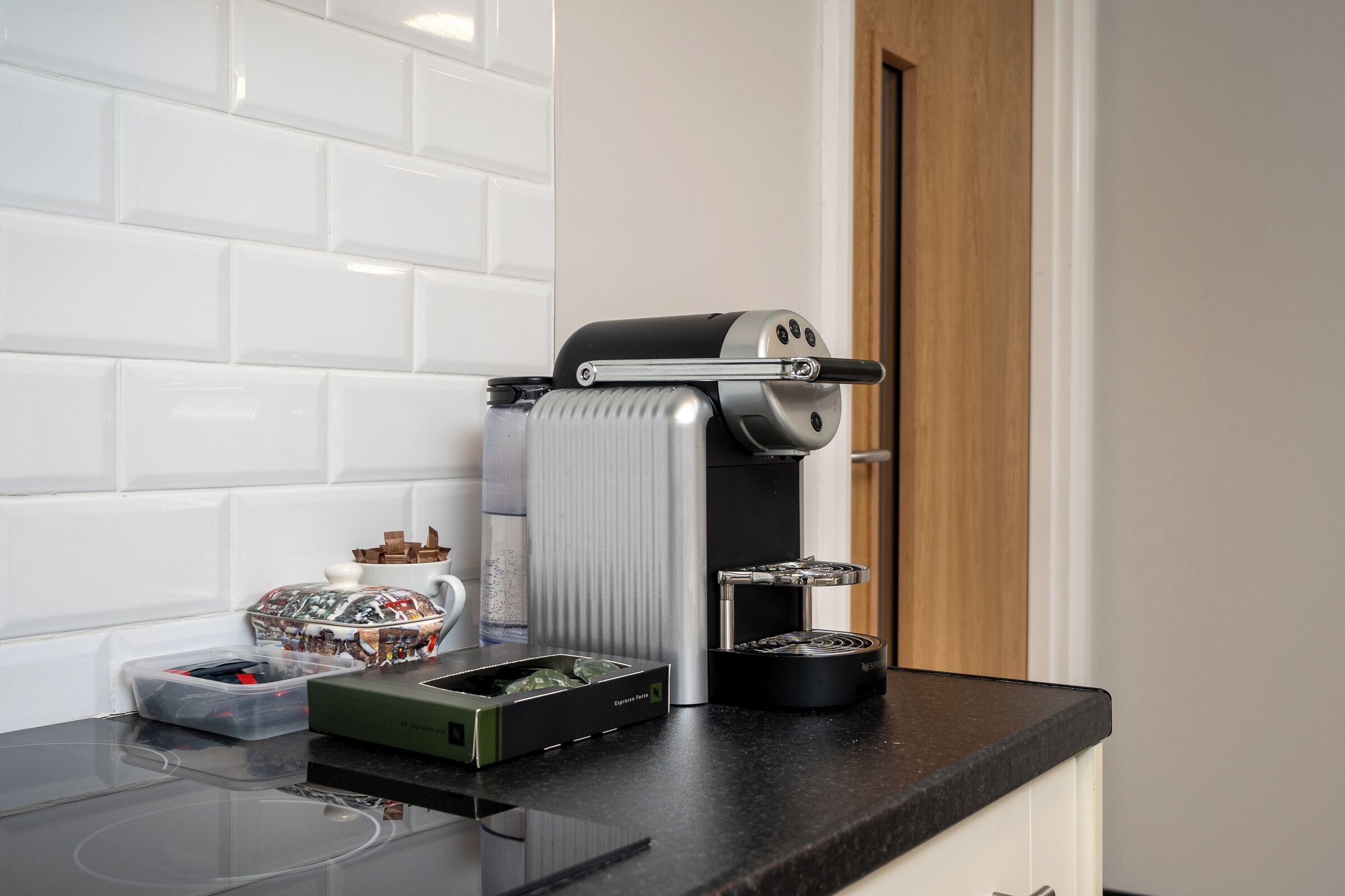 A kitchen with a coffee machine, a kettle, and a container of utensils on the counter.