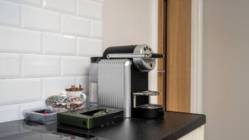 A kitchen with a coffee machine, a kettle, and a container of utensils on the counter.