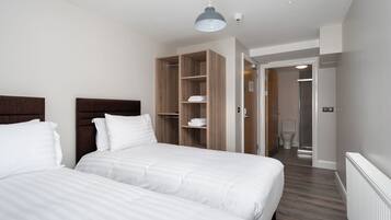 A hotel room with two beds, a wooden wardrobe, a shower, and a toilet.