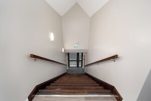 Una escalera de madera con barandales que conduce a una puerta con un letrero verde encima.