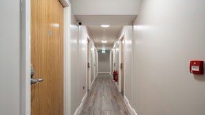 Un pasillo con puertas de madera, un extintor y una luz de emergencia roja en la pared.