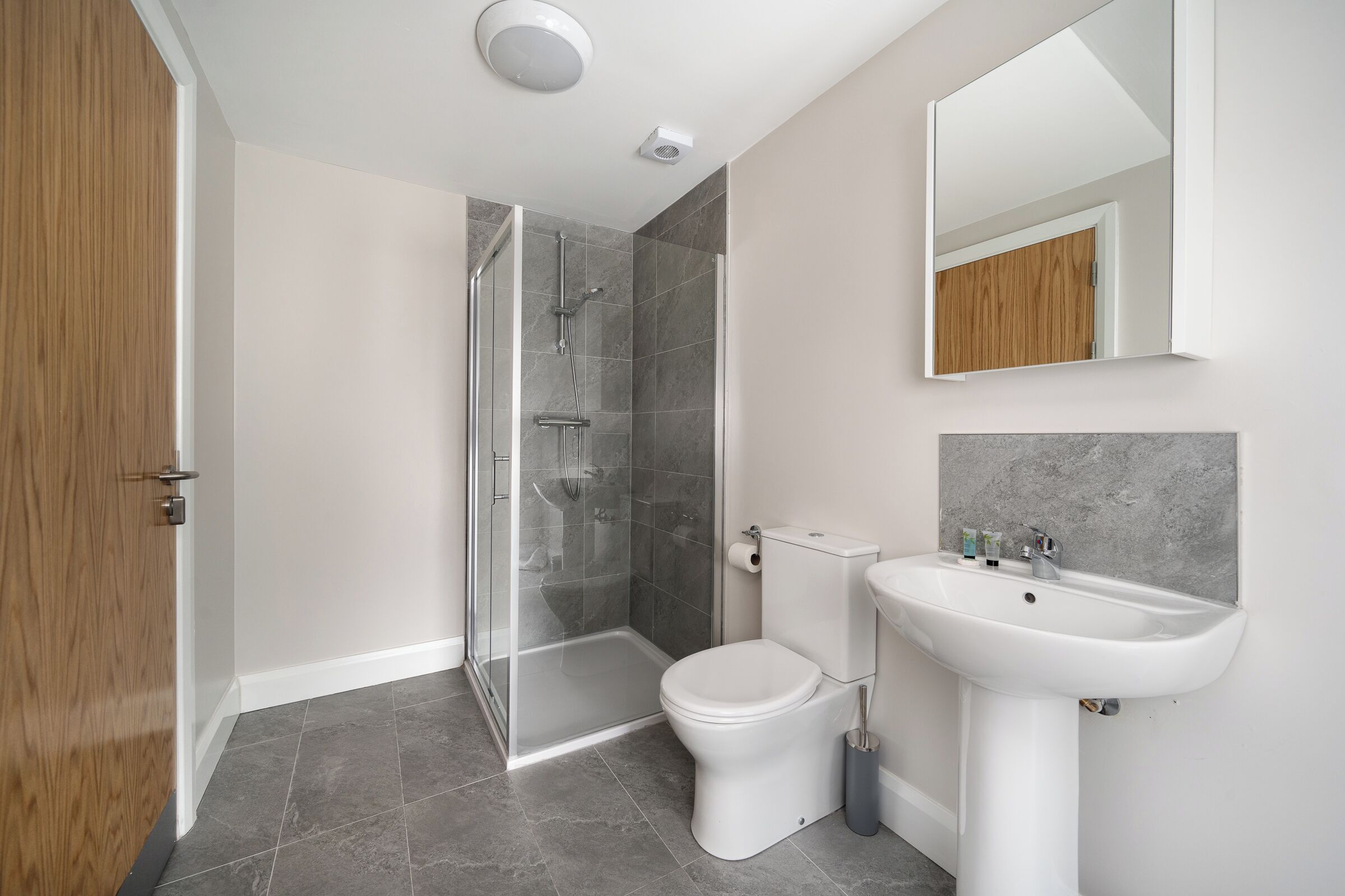 Un baño moderno con cabina de ducha de vidrio, inodoro blanco y lavamanos pedestal.