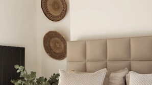 A bedroom with a tufted headboard, two woven wall decorations, a potted plant, and a bed with white pillows. - Sophisticated Notting Hill 2bed (London)