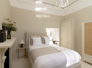 A bedroom with a large bed, bedside tables, a nightstand, a chandelier, and a door. - Sophisticated Notting Hill 2bed (London)