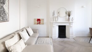 A living room with a white fireplace, a sofa, and a painting on the wall. - Sophisticated Notting Hill 2bed (London)