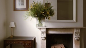 A room with a fireplace, a framed architectural drawing, a vase with flowers, a lamp, and a wicker basket. - Kings Road 3 bed House Chelsea (London)