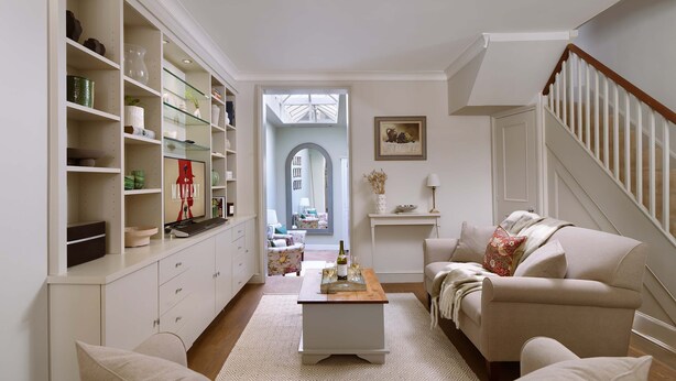 A spacious living room with a sofa, coffee table, and built-in shelving. A staircase is visible in the background. - Kings Road 3 bed House Chelsea (London)